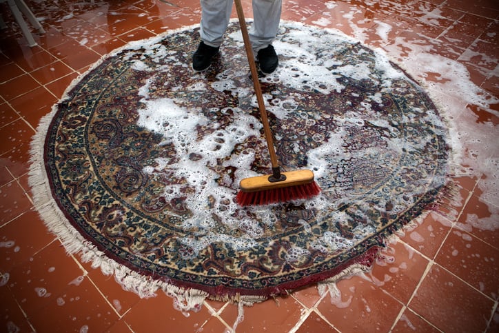 Man washing a rugs on the tile floor.